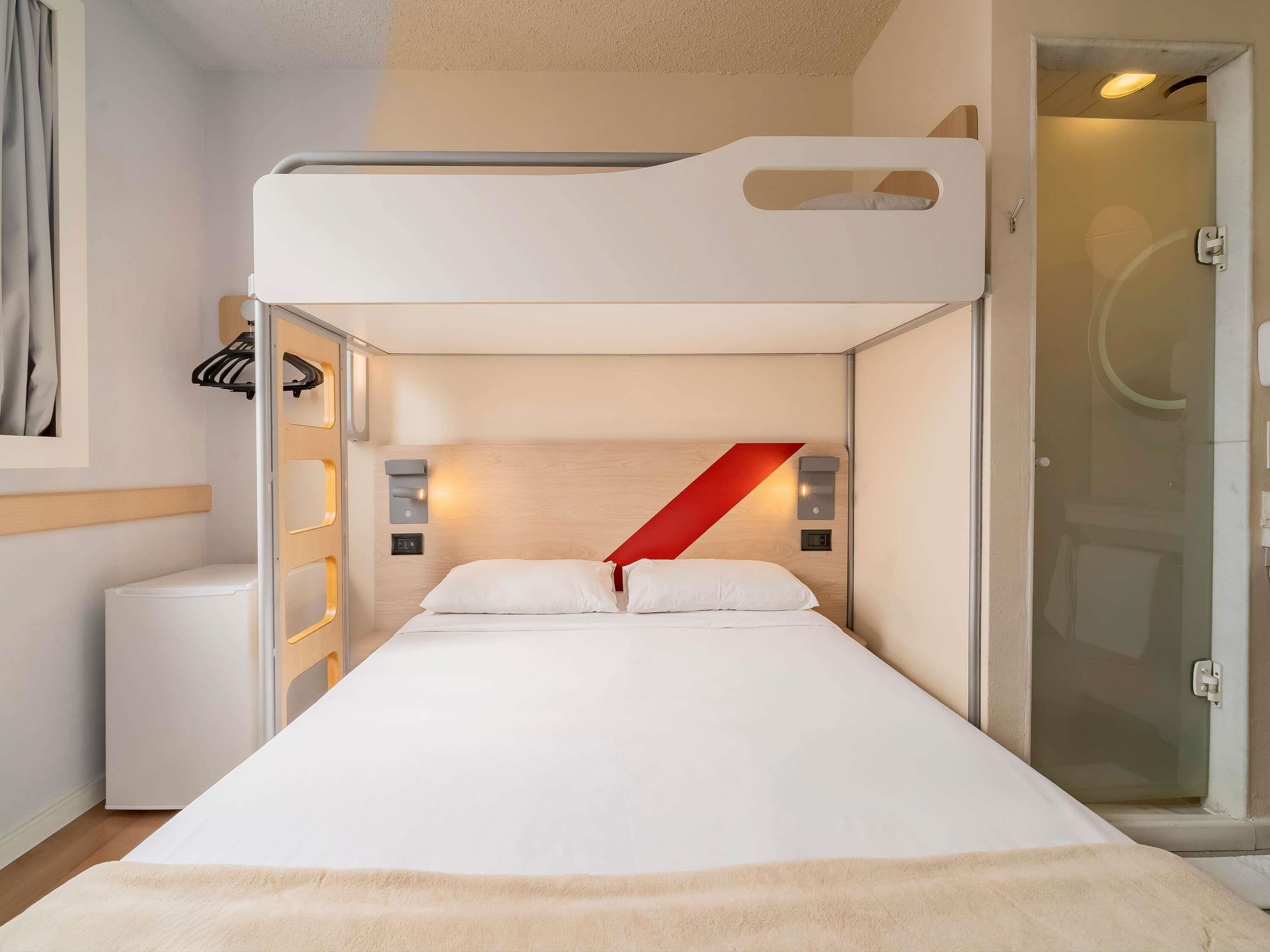 A bunk bed room with a white headboard, a red accent wall, and a glass shower door.