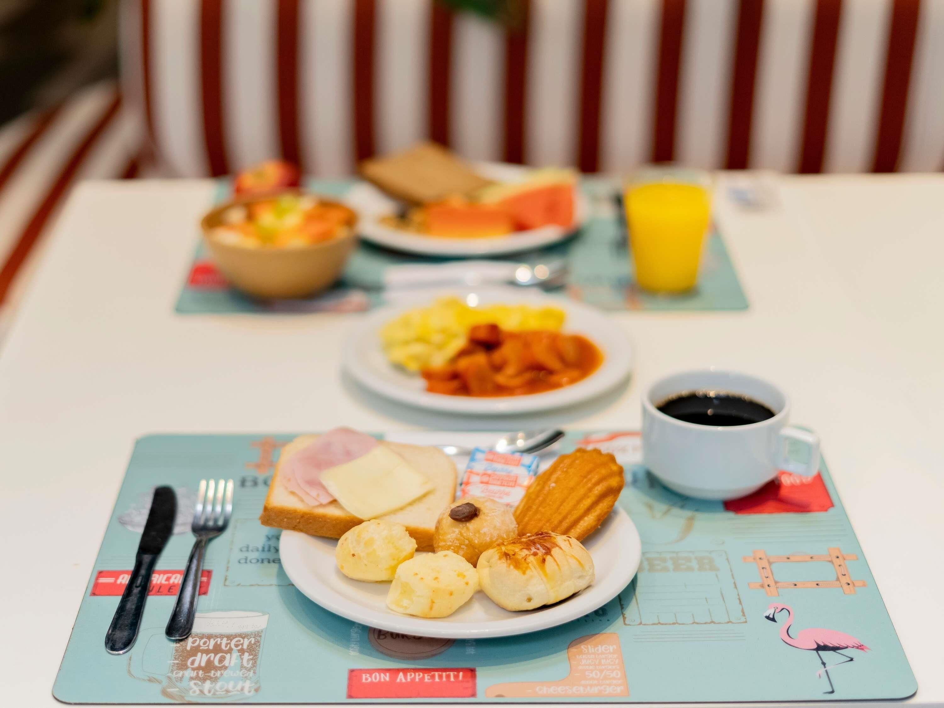 A breakfast setting with a plate of food, a cup of coffee, and a bowl of fruit on a table.