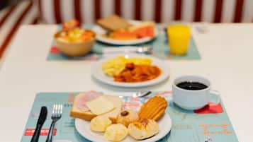 Mesa posta para o café da manhã, com um prato de comida, uma xícara de café e uma tigela de frutas.