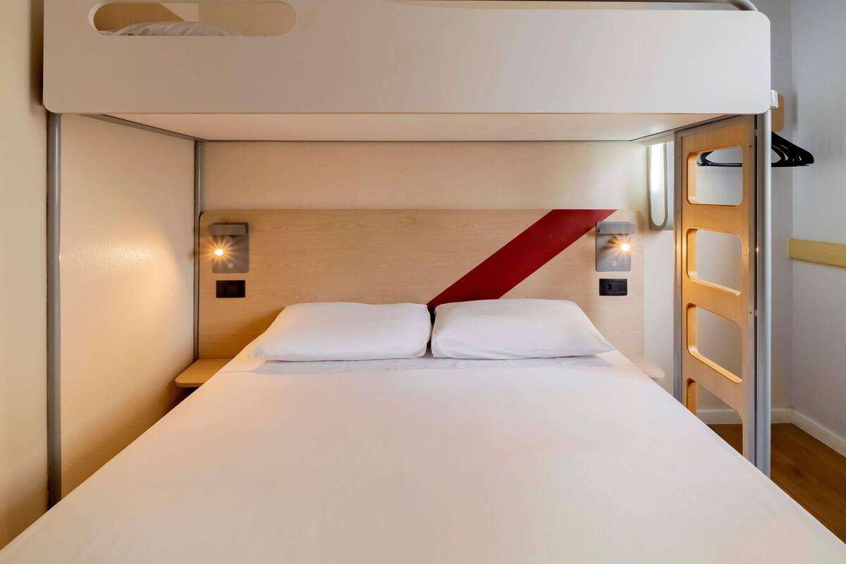 A bunk bed with a wooden headboard, two bedside tables with wall-mounted lamps, and a red accent wall.