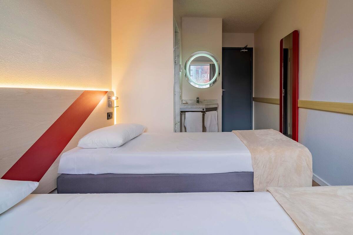 A hotel room with a bed, a bedside table, a mirror, and a bathroom visible through an open door.