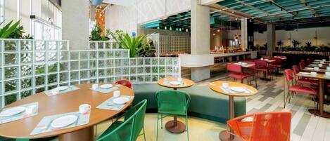 A modern dining area with round tables, green and orange chairs, and a high ceiling with exposed beams.