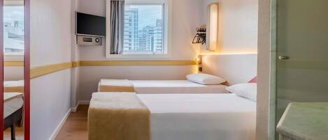 Habitación de hotel con dos camas, un televisor montado en la pared, una ventana con cortinas y un baño con lavamanos y espejo.