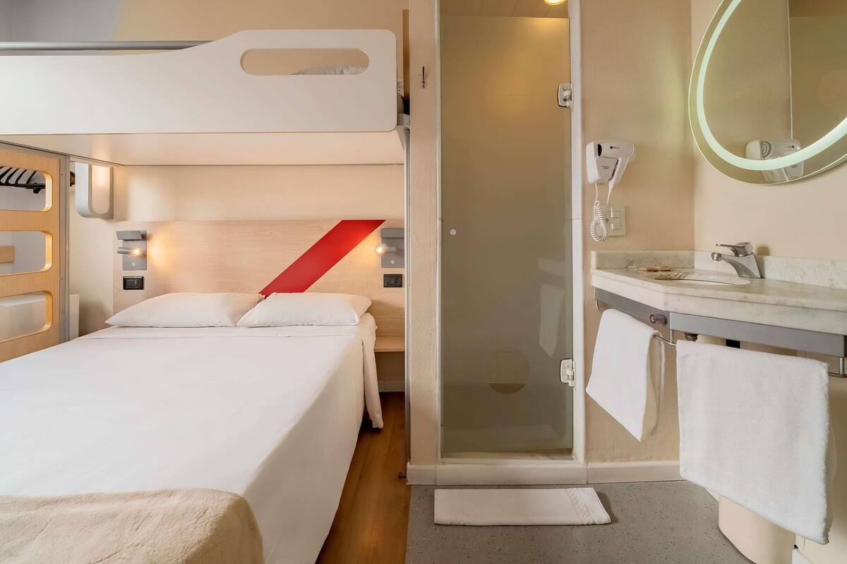 A hotel room with a bed, a shower, a bathroom with a sink and mirror, and a towel rack.
