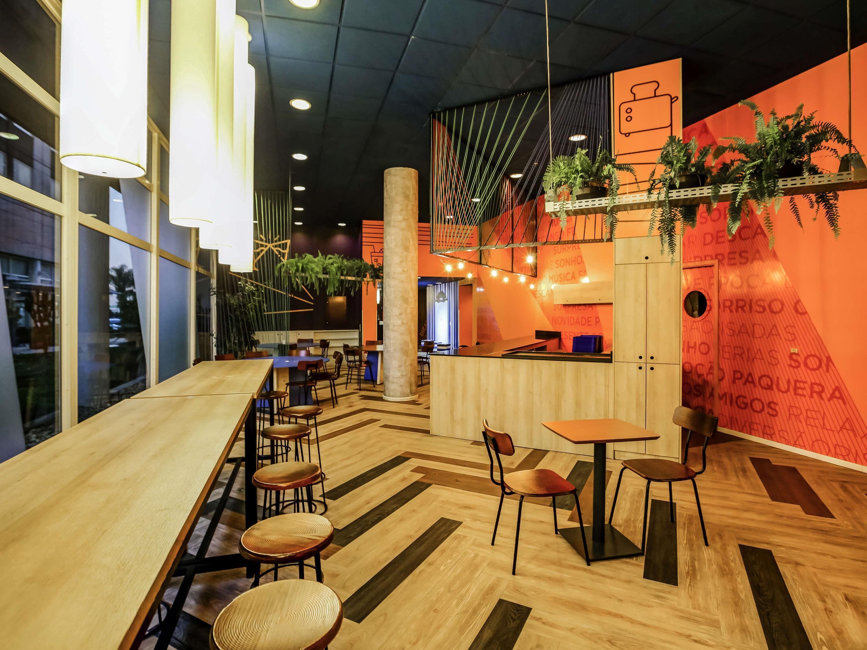 Ein modernes Interieur mit Holztischen und -stühlen, einer zentralen Säule und dekorativen Pflanzen.