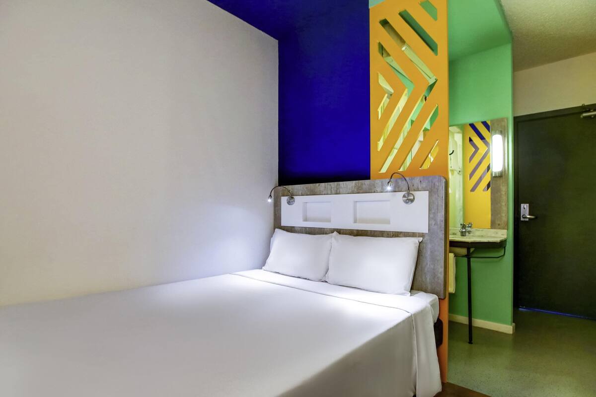 A single bed with a headboard, a bedside table, a mirror, and a small sink in a room with a green wall and a blue accent wall.