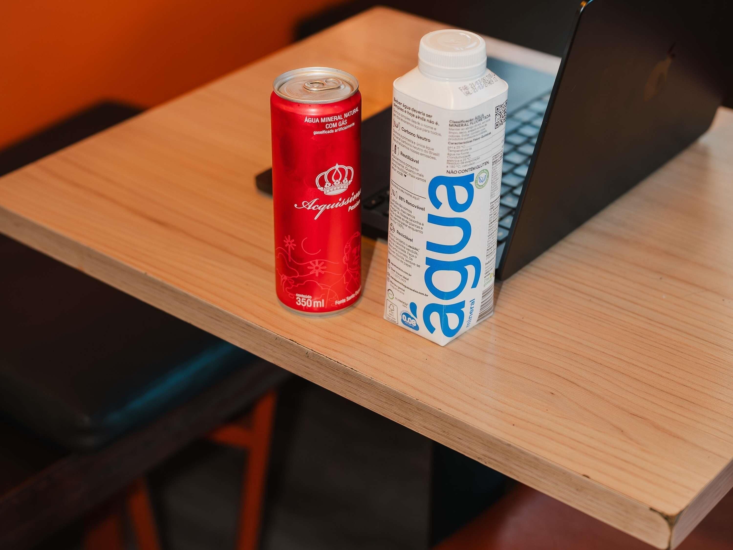 Una lata de agua mineral y una botella de agua junto a una computadora portátil sobre una mesa de madera.