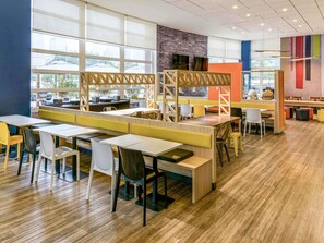 Un espace repas moderne avec des tables hautes et des banquettes, de grandes fenêtres et un mur décoratif en briques.
