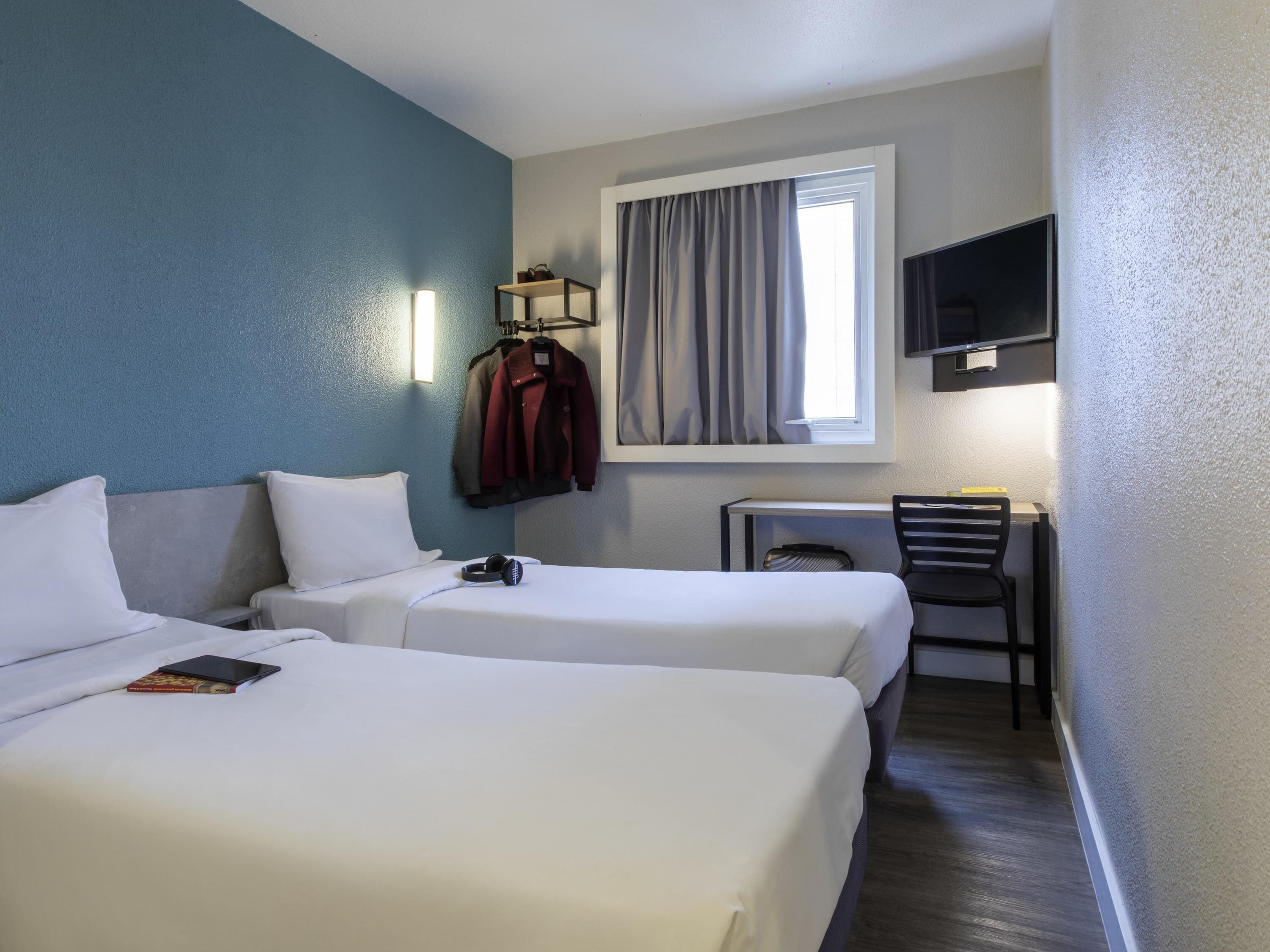 Habitación de hotel con dos camas, un escritorio, una silla, un televisor y una ventana con cortinas.