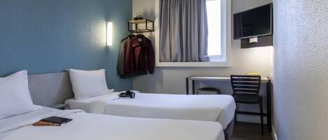 Habitación de hotel con dos camas, un escritorio, una silla, un televisor y una ventana con cortinas.