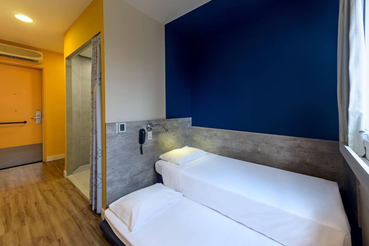 A hotel room with a bed, a bathroom with a shower, and a door.