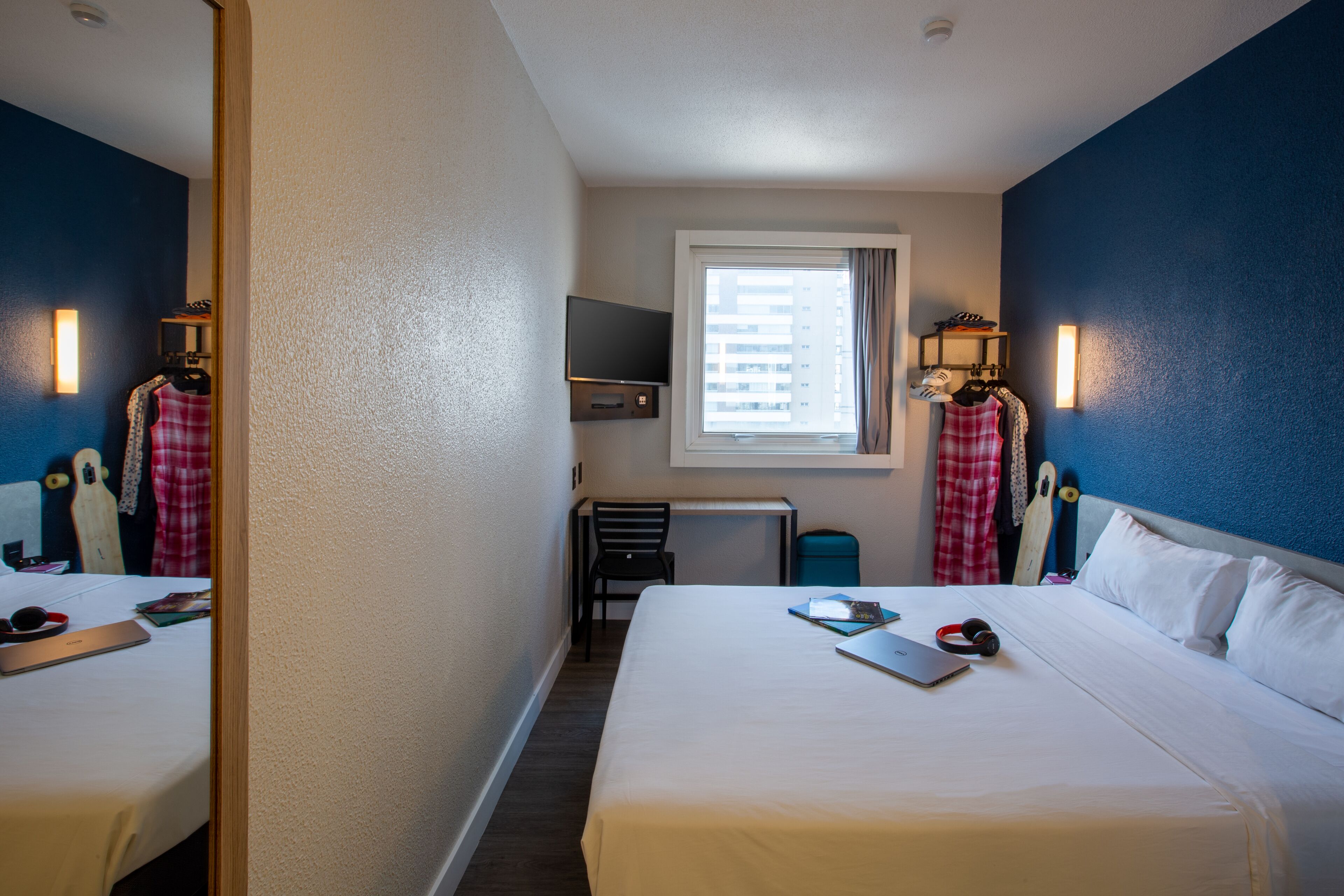 A hotel room with two beds, a TV, a window with curtains, and a desk with a chair.