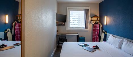 A hotel room with two beds, a TV, a window with curtains, and a desk with a chair.