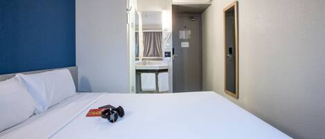 A hotel room with a bed, a desk, and an air conditioning unit.
