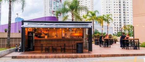 Un restaurante con terraza, barra y vista a edificios altos al fondo.