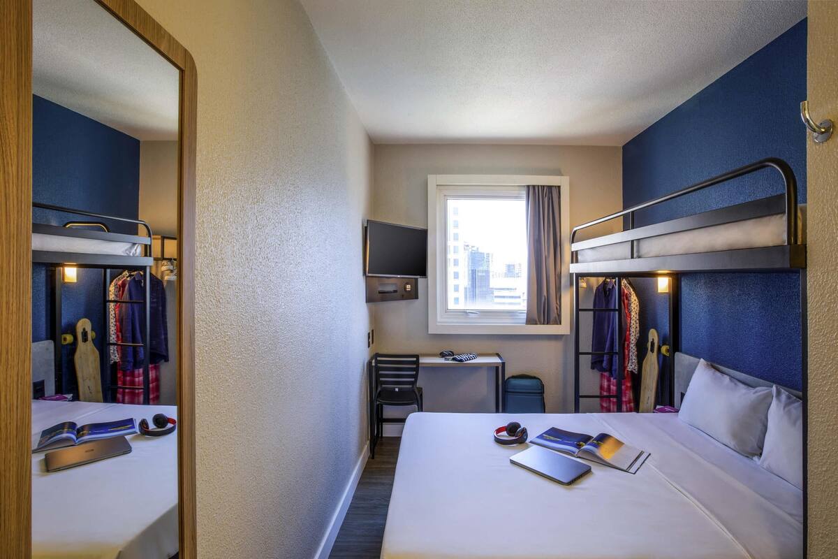 A compact hotel room with bunk beds, a desk, a chair, and a window with a city view.