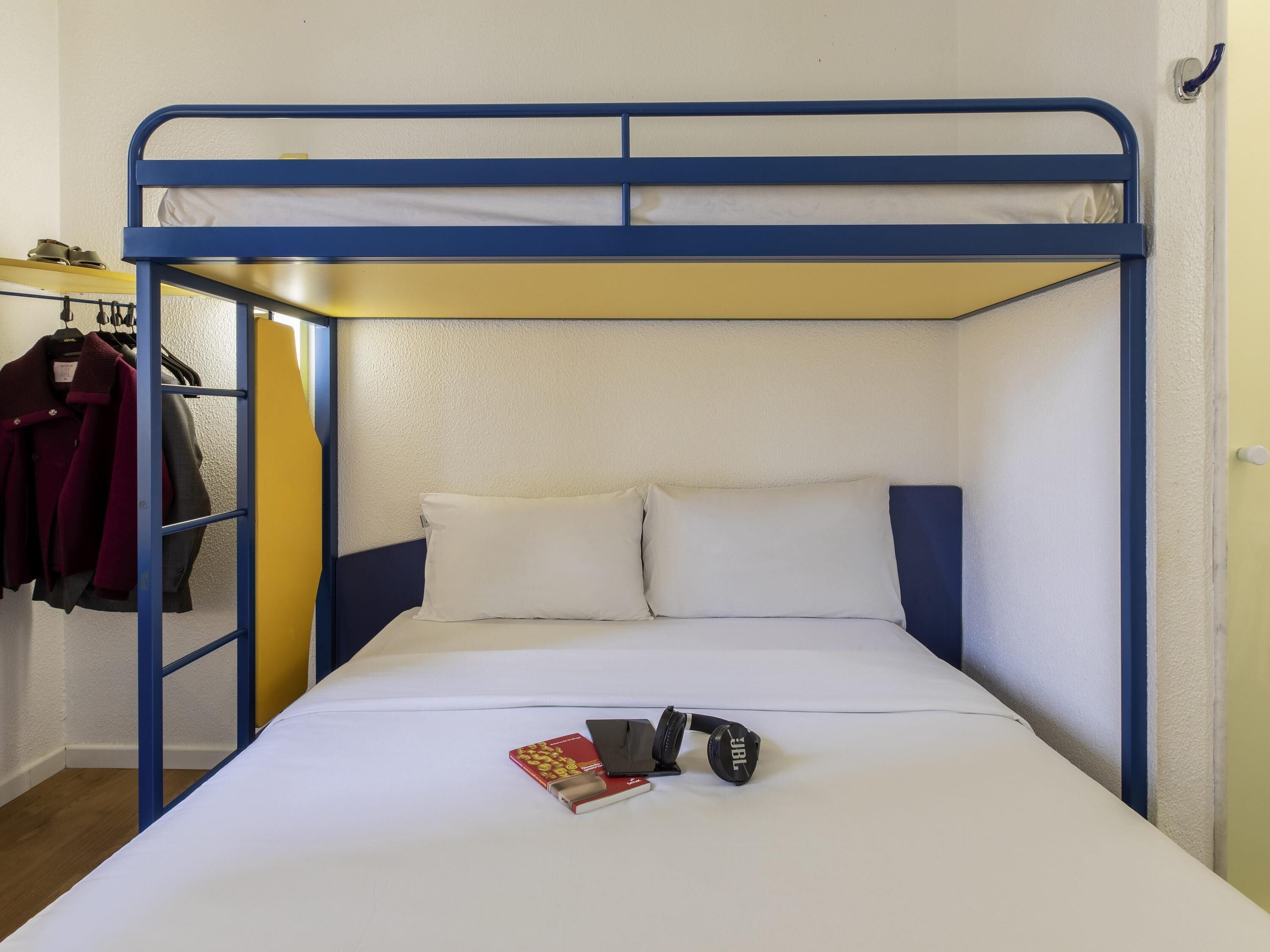 A bunk bed with a blue frame and white bedding. There is a book and a pair of headphones on the bed.