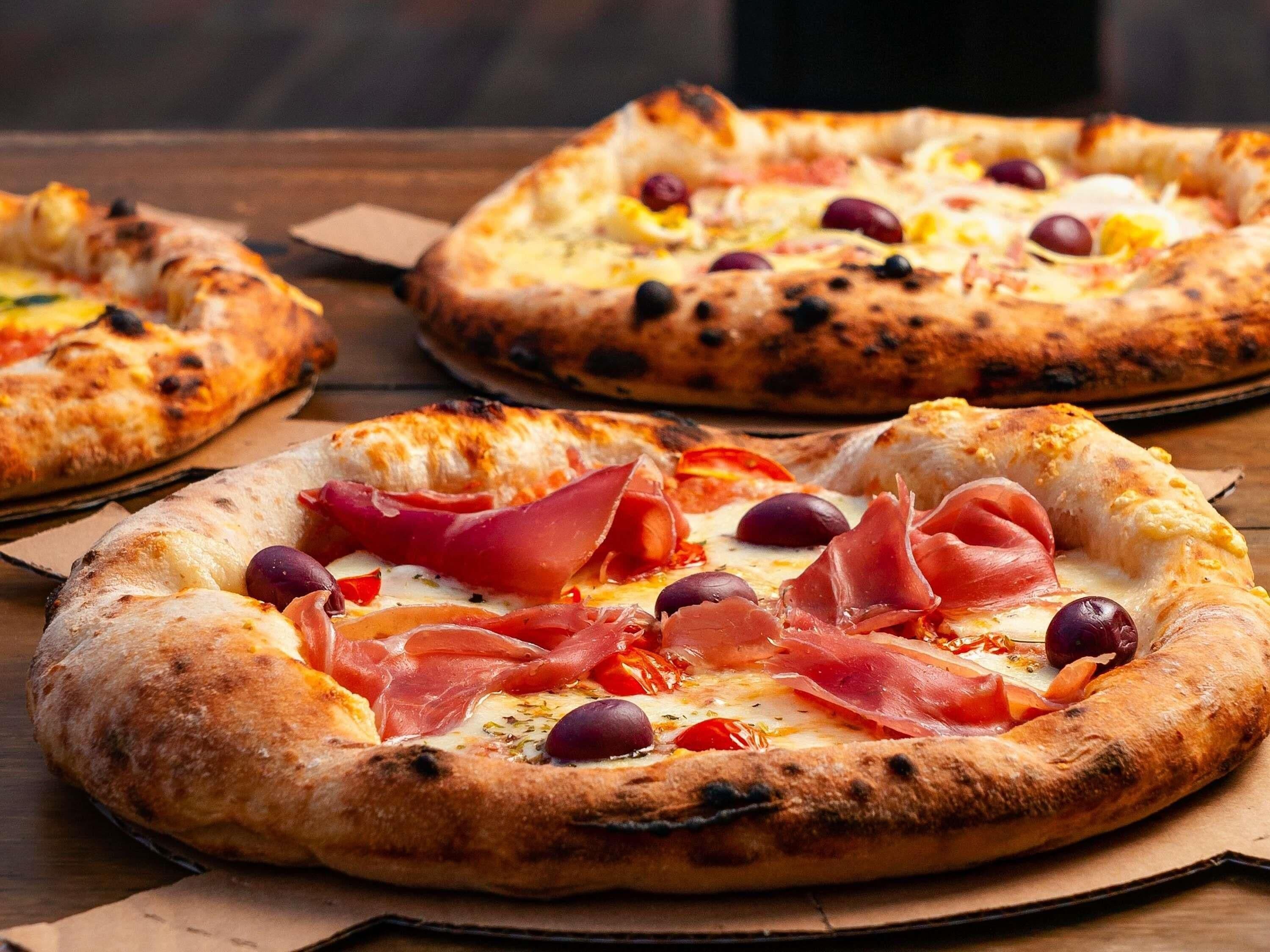 Three pizzas with toppings on a wooden surface.