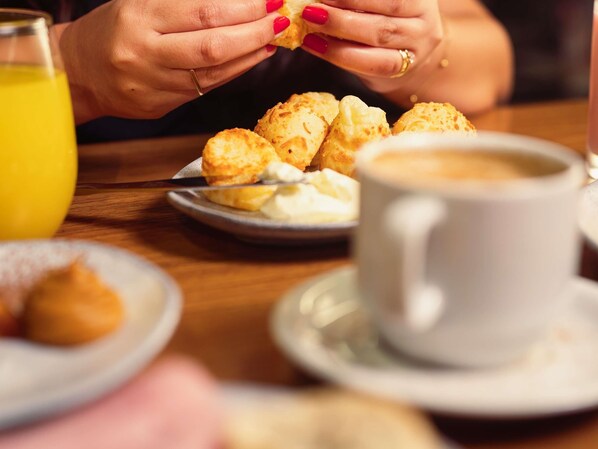 Une personne est assise à une table, tenant un biscuit dans une main, une tasse de café dans l’autre et un verre de jus d’orange.