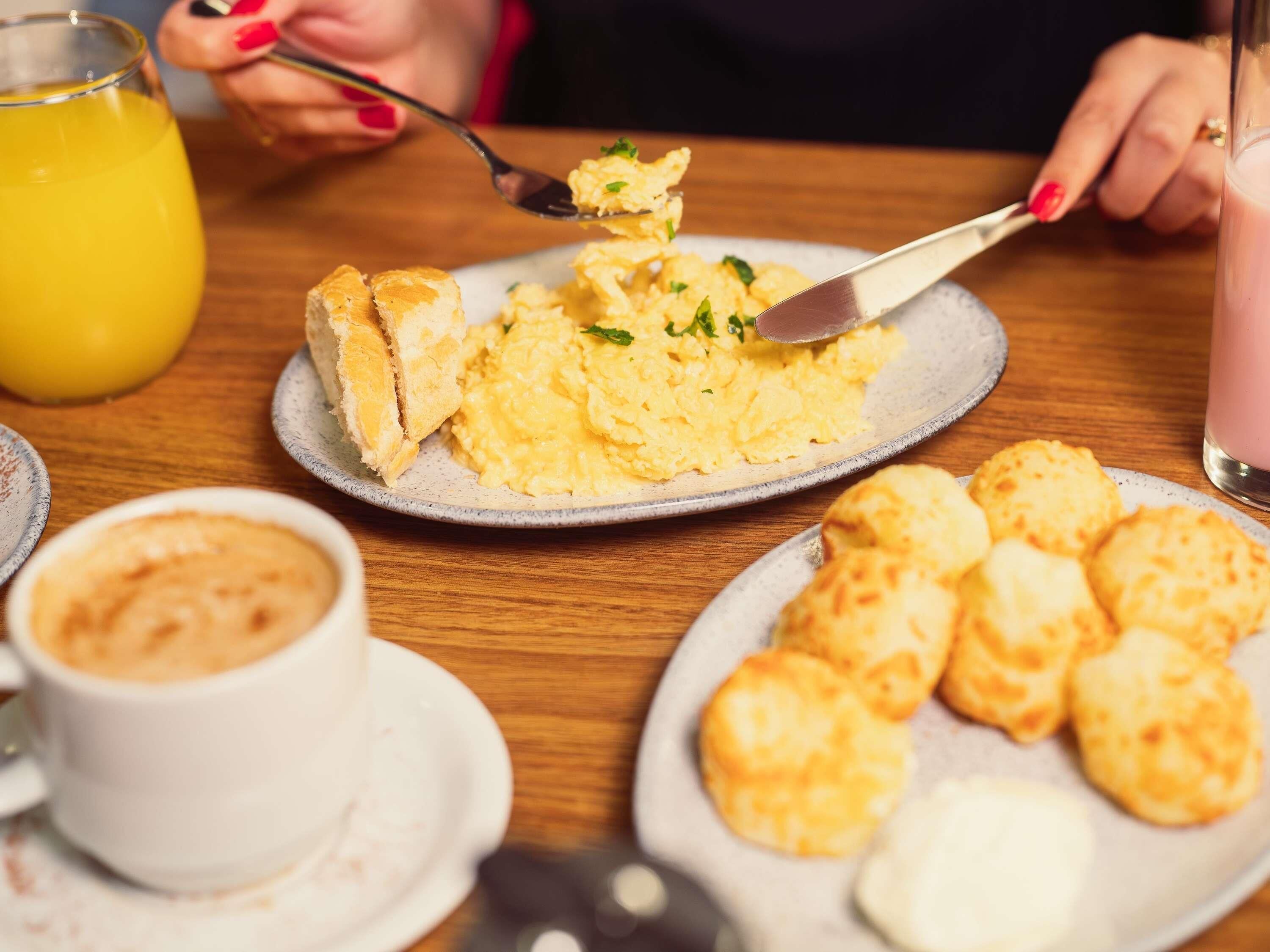 A breakfast setting with scrambled eggs, toast, biscuits, and a glass of orange juice.