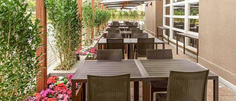 An outdoor patio with tables and chairs, surrounded by plants and flowers.