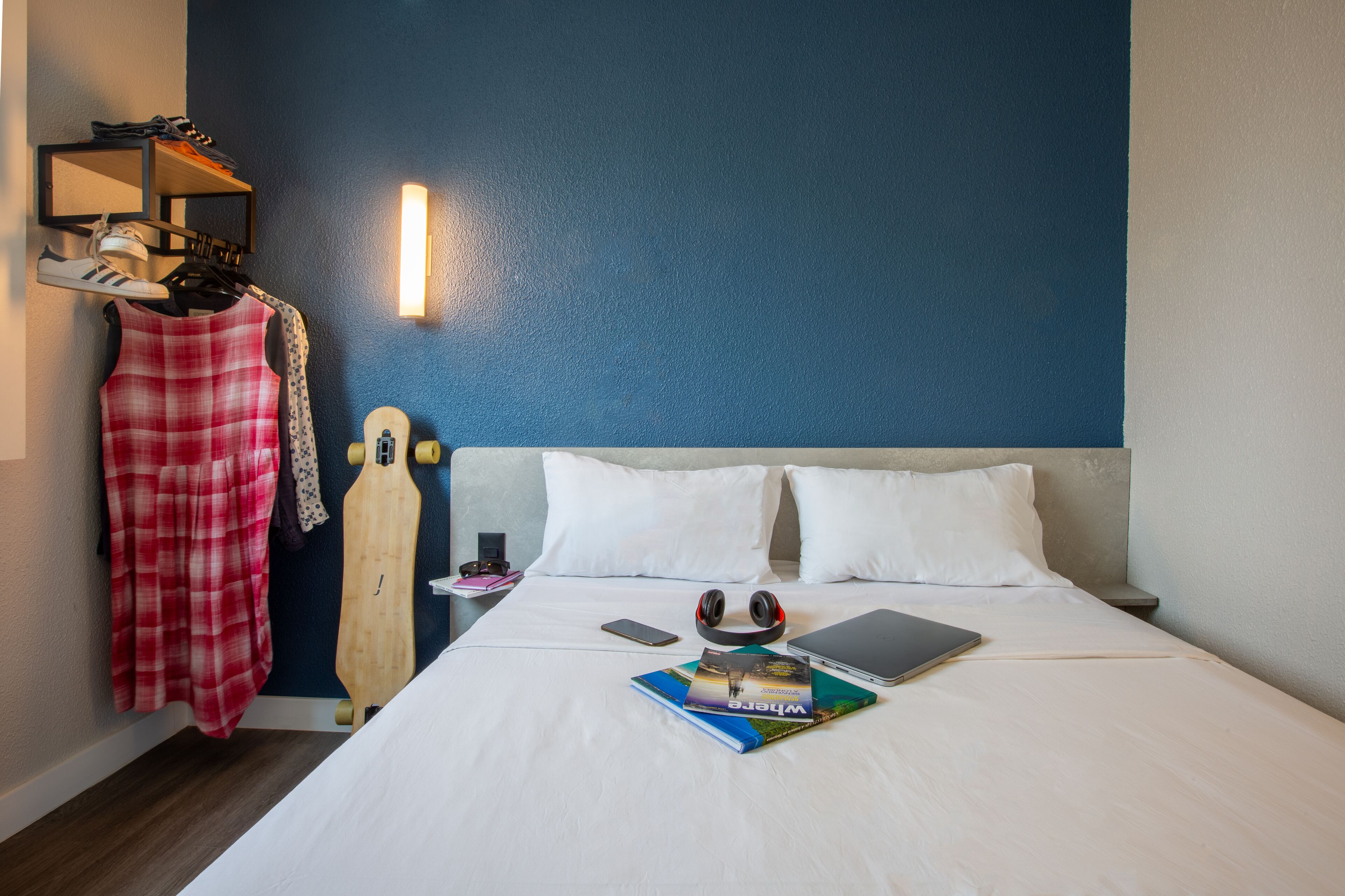A neatly made bed with white linens, a pair of headphones, a laptop, and a book titled "Where to Go."