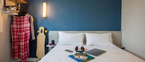 A neatly made bed with white linens, a pair of headphones, a laptop, and a book titled "Where to Go."