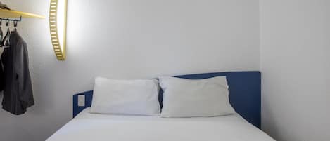 Una cama bien hecha con ropa blanca, un cabecero azul y un par de auriculares sobre la cama.