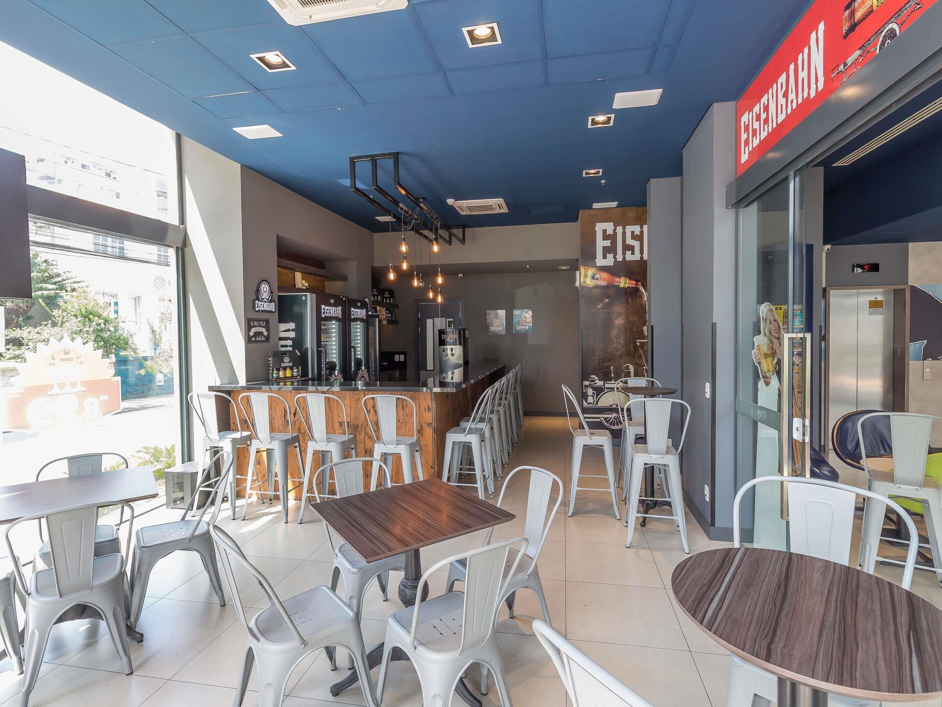 Interior de café com várias mesas, cadeiras, um balcão e um elevador visível.