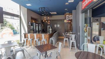 Interior de café com várias mesas, cadeiras, um balcão e um elevador visível.