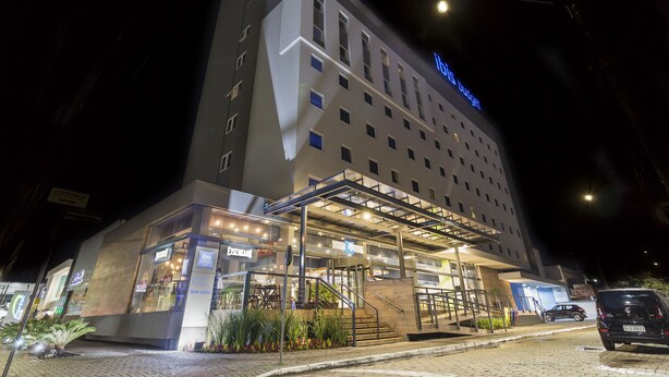 Hotel com design moderno, destacando uma entrada imponente com galeria coberta e escadaria visível para a recepção.
