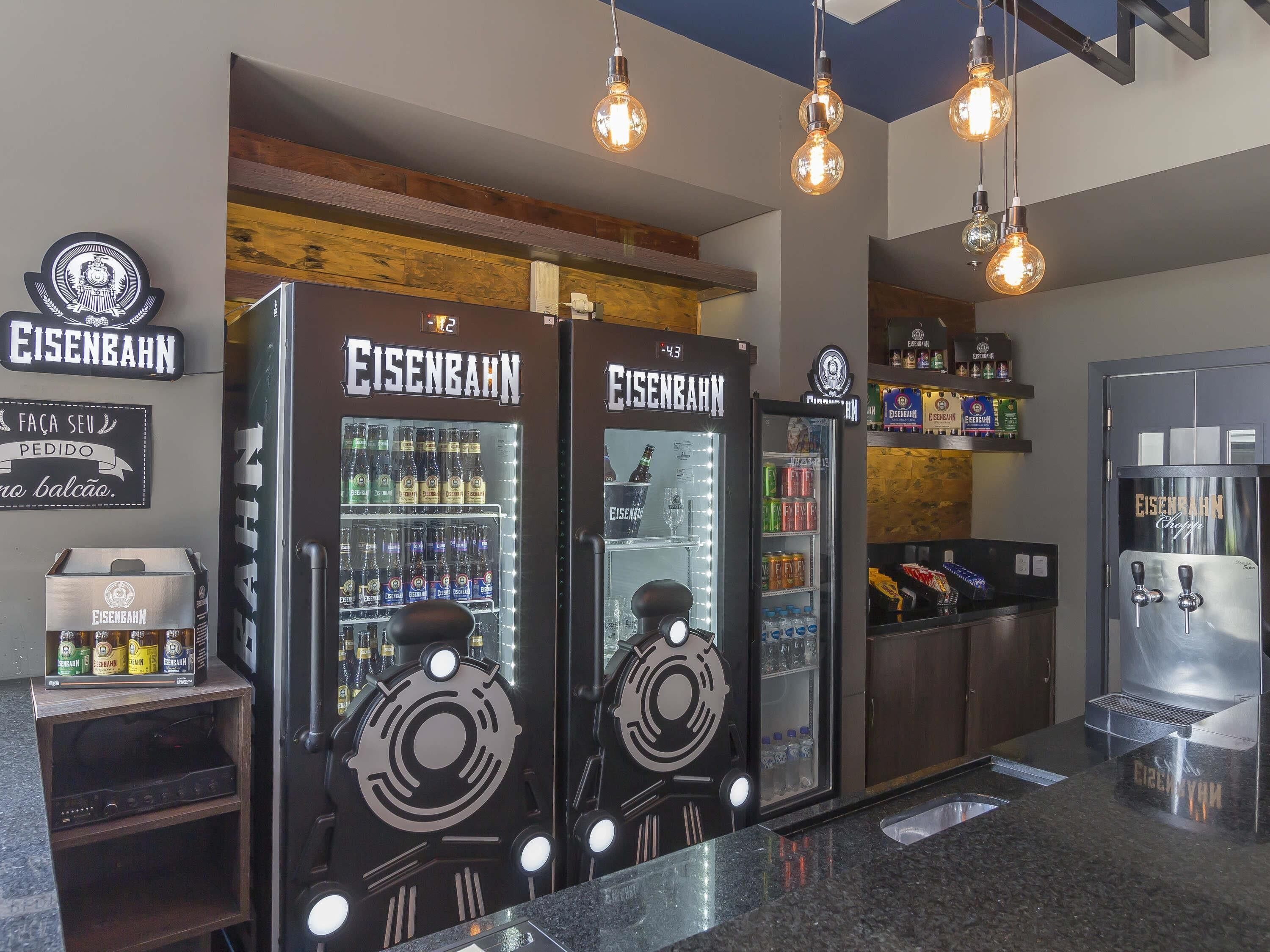 Zona de bar con varias neveras de marca Eisenaahn, una selección de bebidas y un mostrador con caja registradora.