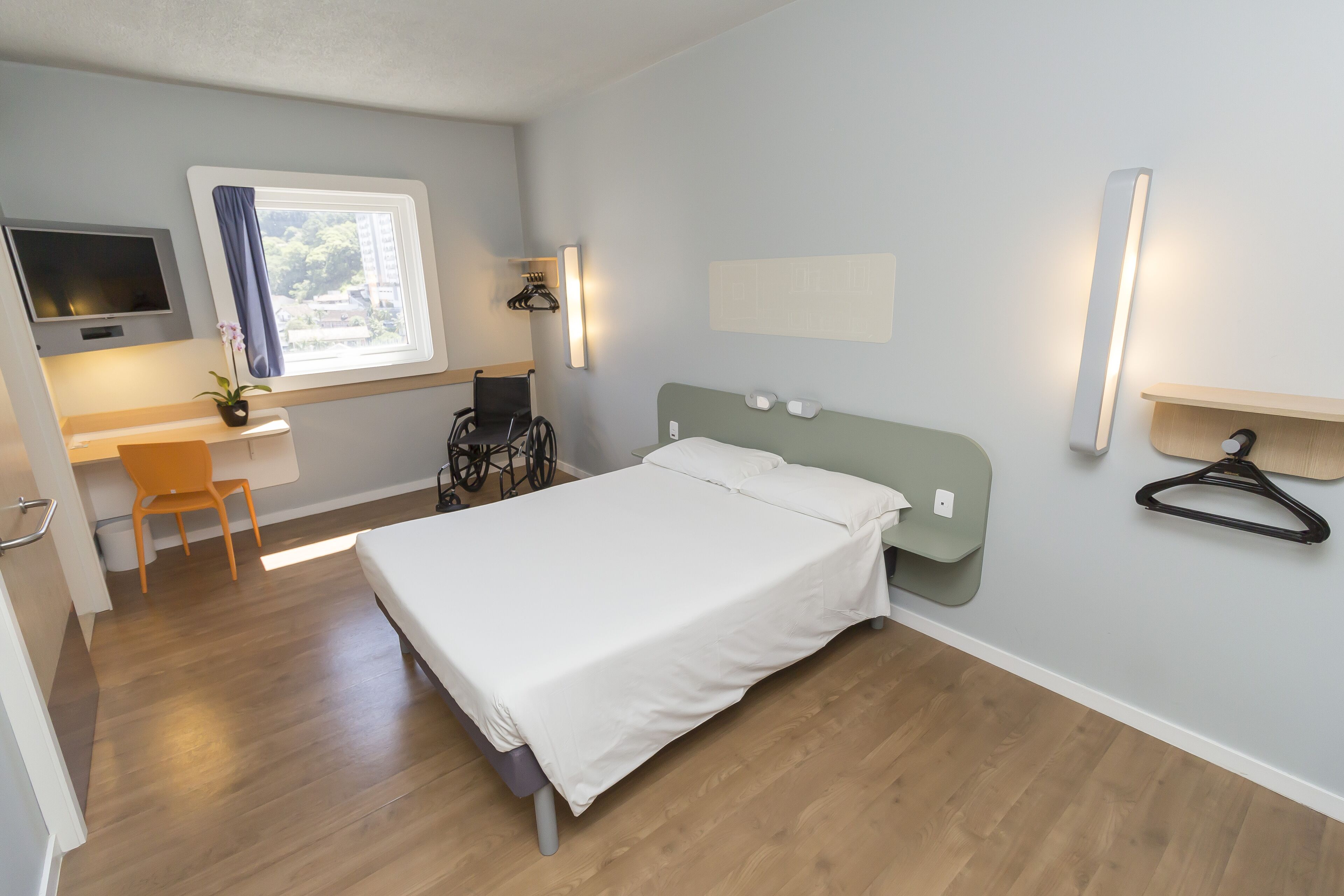 Ein modernes Schlafzimmer mit einem Bett, einem Schreibtisch, einem Stuhl, einem Fernseher und einem Fenster mit Vorhängen.