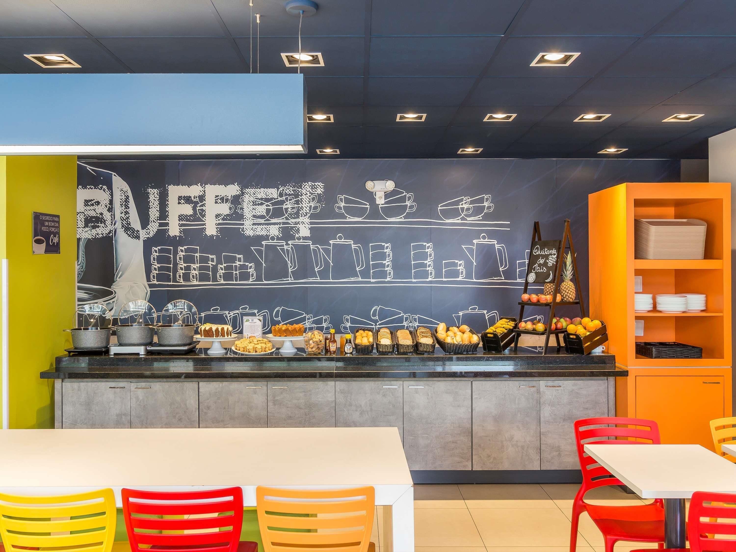 A cafe interior with a chalkboard menu, a buffet counter, and colorful chairs.