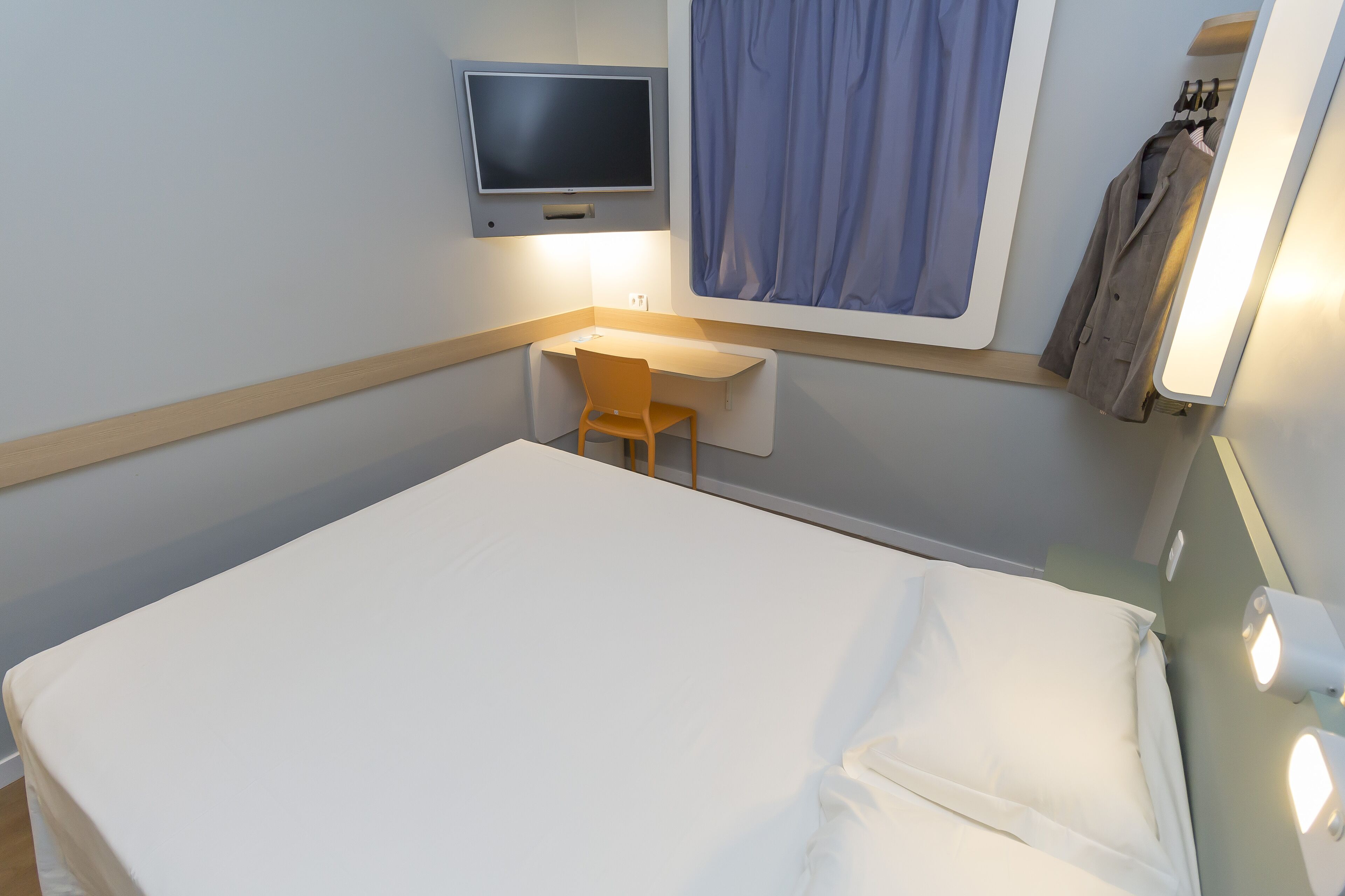 A hotel room with a bed, a desk, a chair, a television, and a window with curtains.