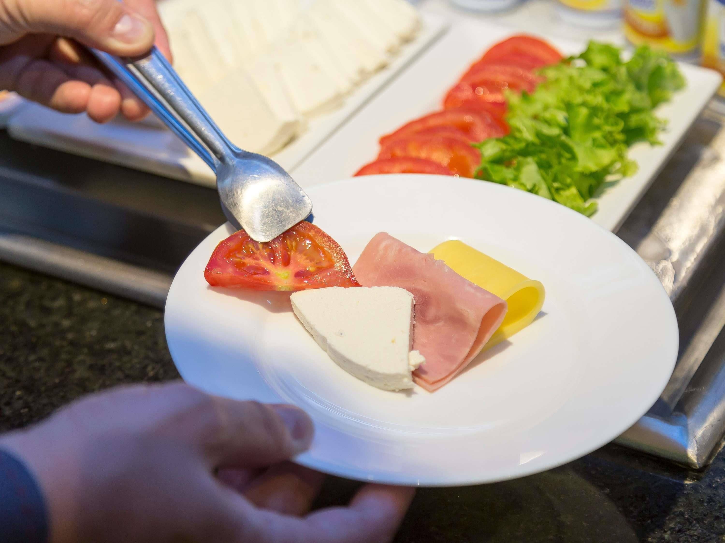 Um prato com uma fatia de tomate, um pedaço de queijo e uma fatia de presunto.