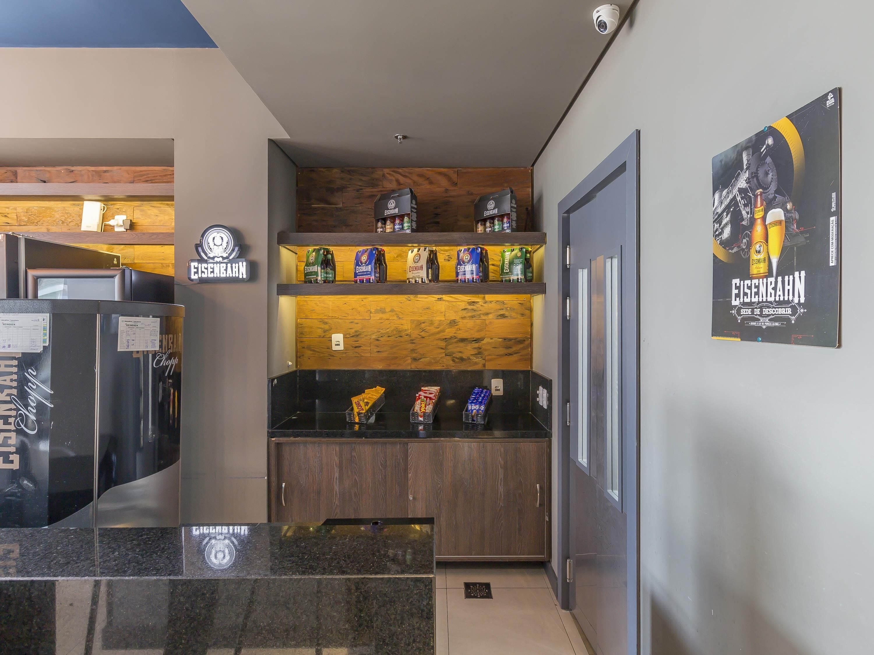 Un espace bar moderne avec un mur en bois, des étagères remplies de collations et une affiche représentant une bouteille de bière.