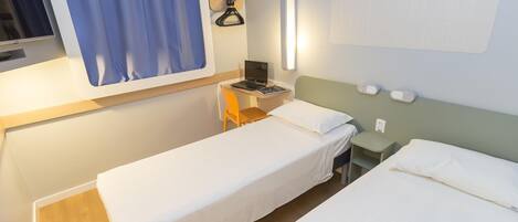 Habitación de hotel con dos camas, un escritorio con una laptop, un televisor y una lámpara fijada a la pared.