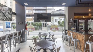 Um café moderno com mesas, cadeiras, uma tela de TV, máquinas de venda automática e vista para a rua.