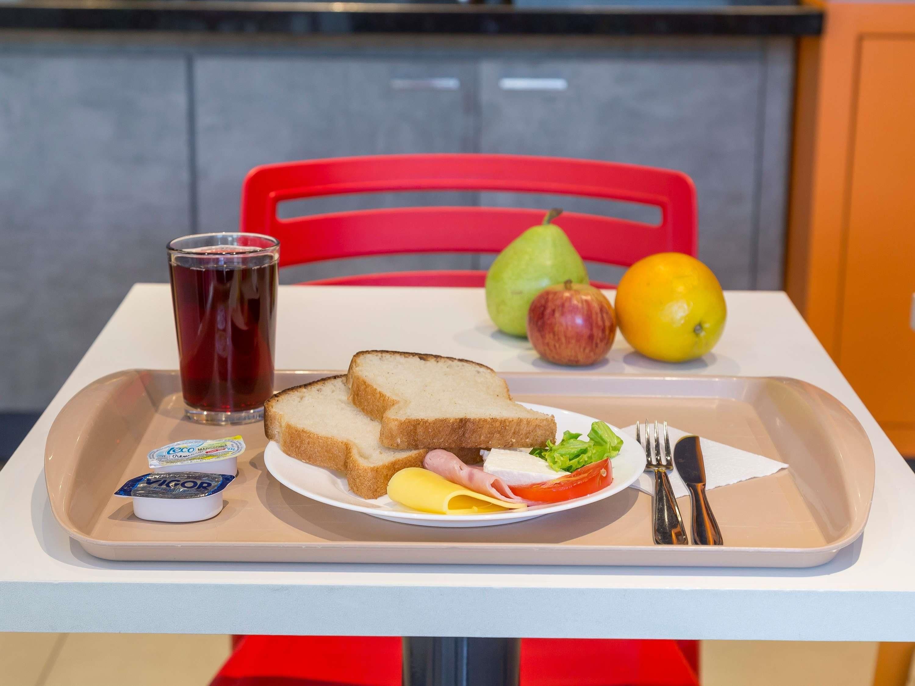 En bakke med en sandwich, et glas drikke og en tallerken med frugt og grøntsager.