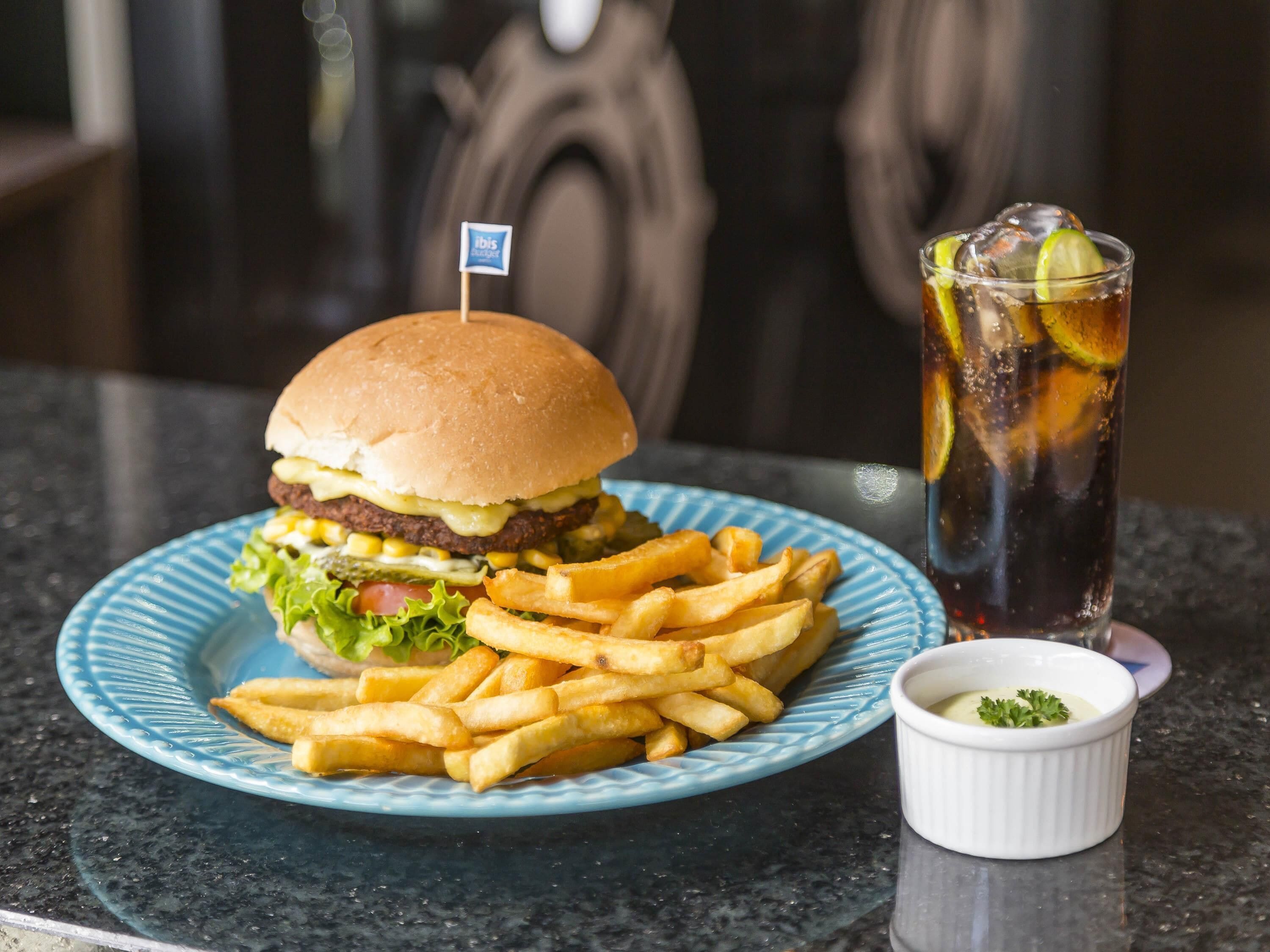 Una hamburguesa con papas fritas y una bebida, sobre un plato azul.