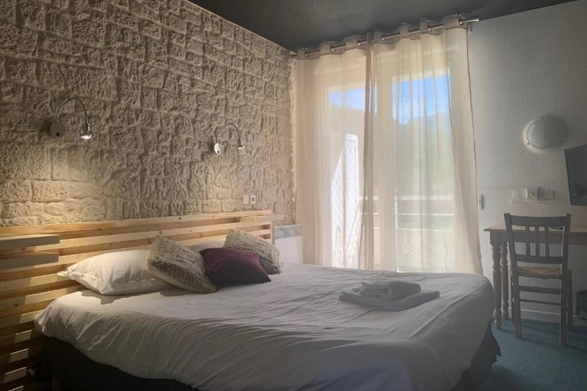 A bedroom with a stone wall, a wooden bed, a desk, and a chair.