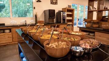 A buffet setup with multiple wooden bowls containing various dishes, a coffee machine, and a clock on the wall.