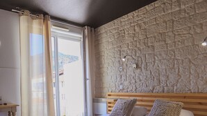 A hotel room with a large bed, a wooden headboard, and a stone-textured wall. -  Les Lavandes (Remuzat)