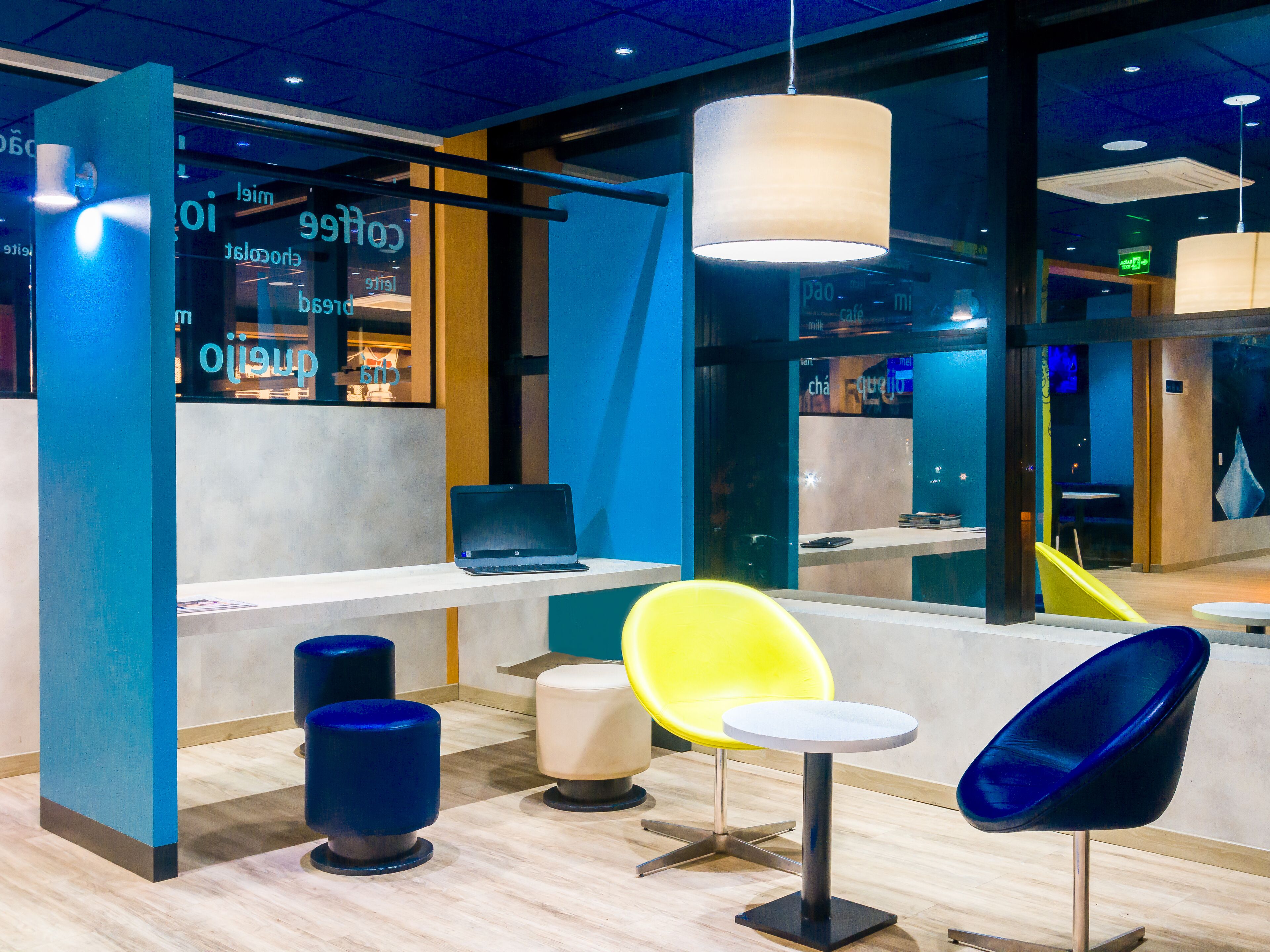 Um interior moderno com um laptop numa mesa, uma cadeira amarela, uma cadeira azul e uma mesa redonda.