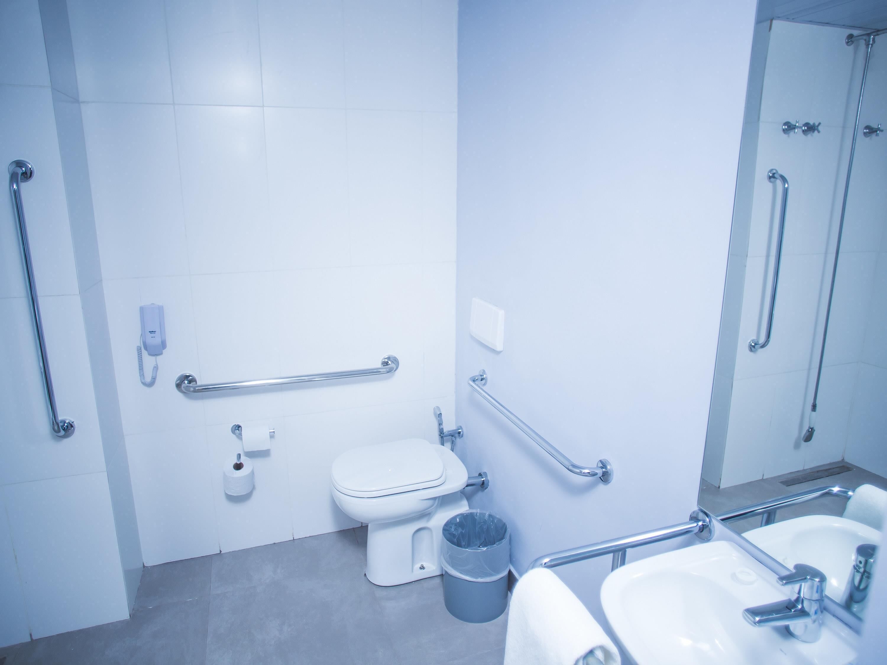 Un baño moderno con inodoro, bidé y lavabo, equipado con barras de apoyo y pasamanos para facilitar el acceso.