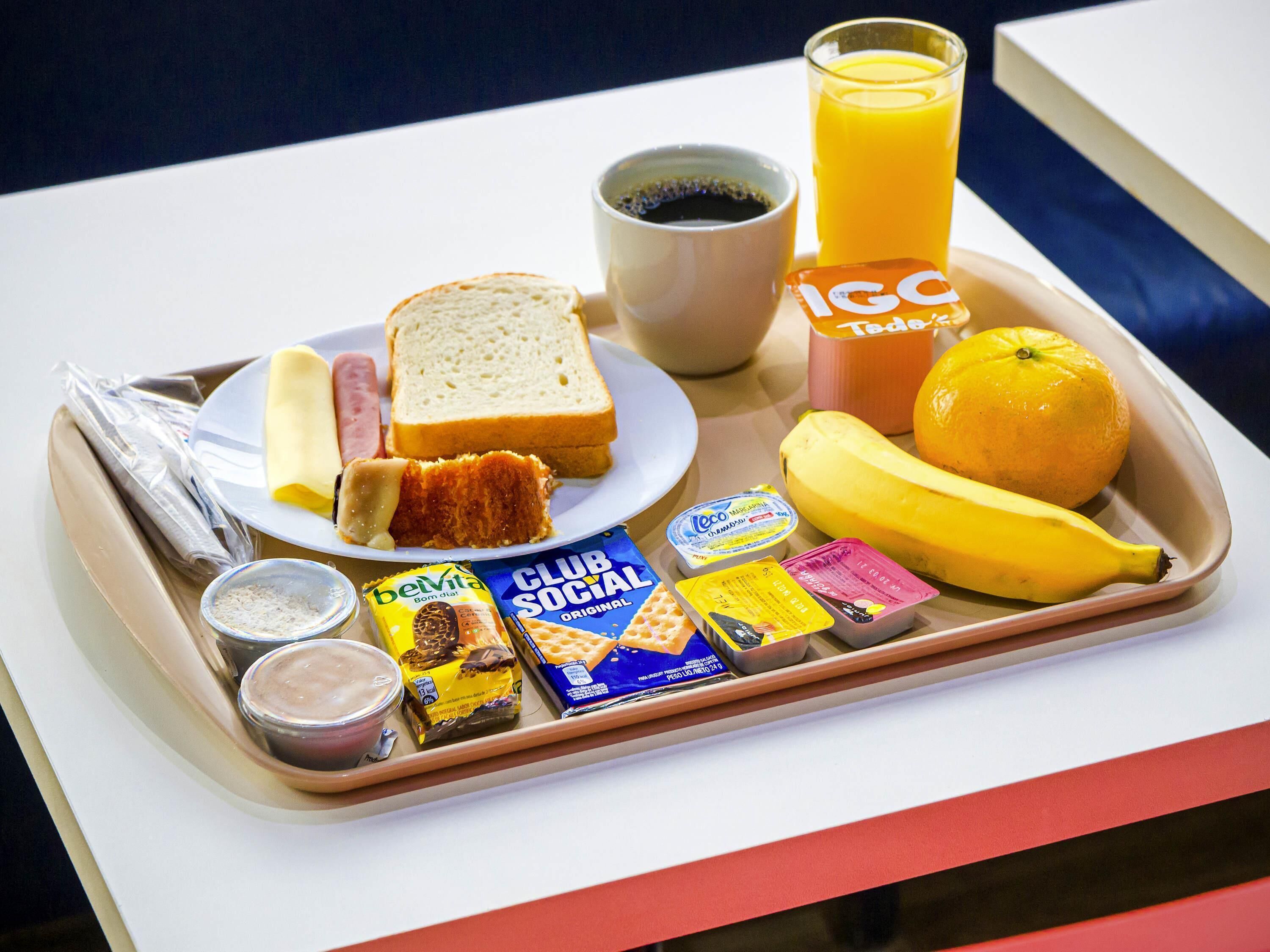 A tray with breakfast items including bread, a banana, an orange, a glass of orange juice, a cup of coffee, and various snacks.