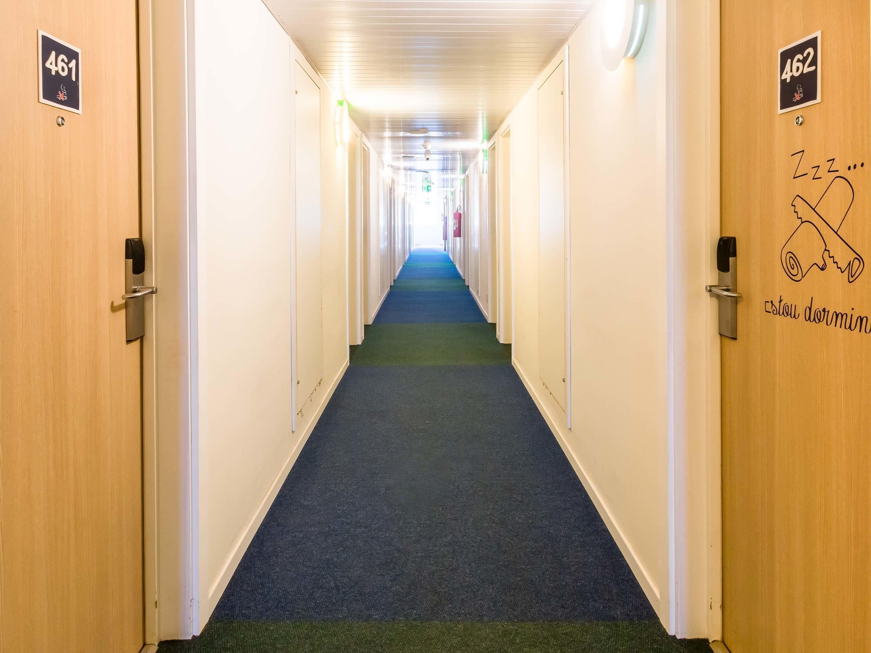 Un pasillo de hotel con puertas numeradas 461 y 462, una alfombra azul y un cartel en la puerta 462 que dice 'Zzz... estoy durmiendo'.