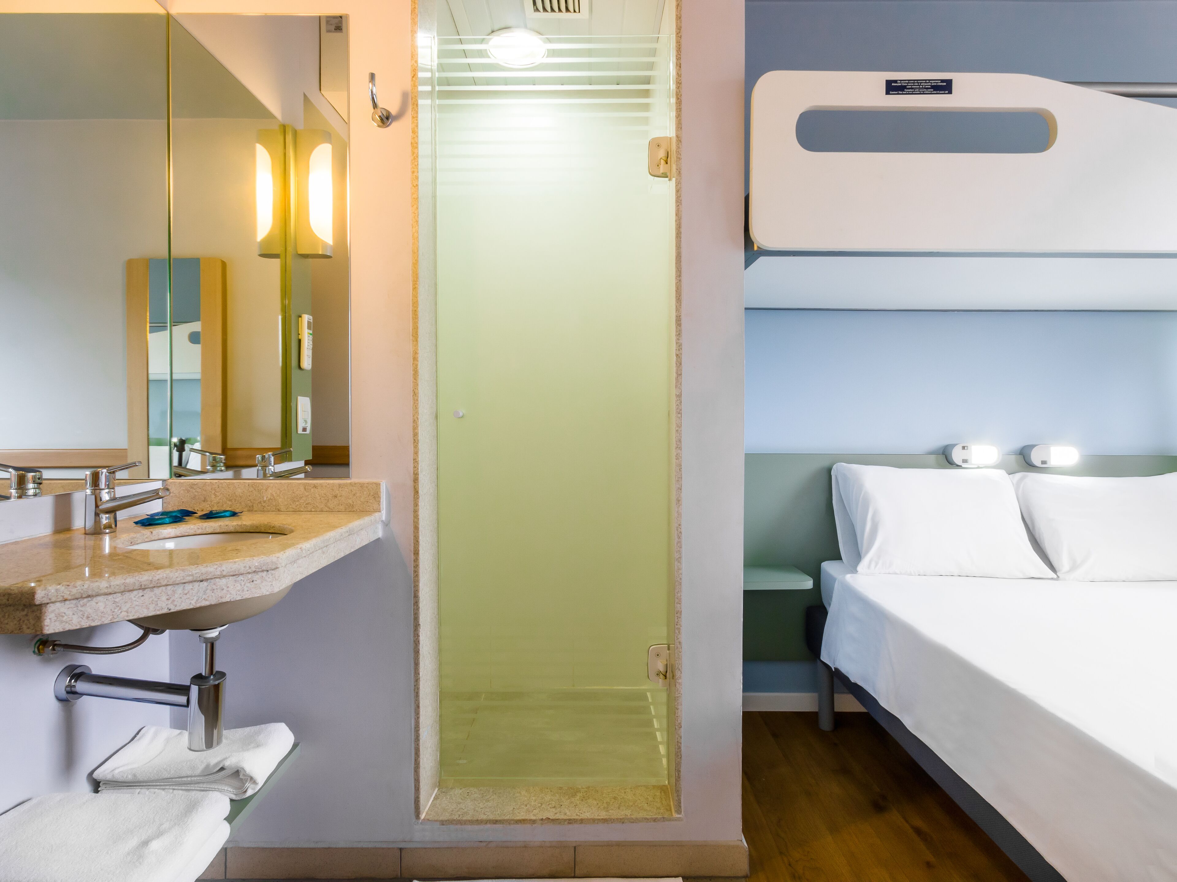 Una camera d'albergo con bagno, lavandino, specchio, asciugamano e letto con biancheria bianca.