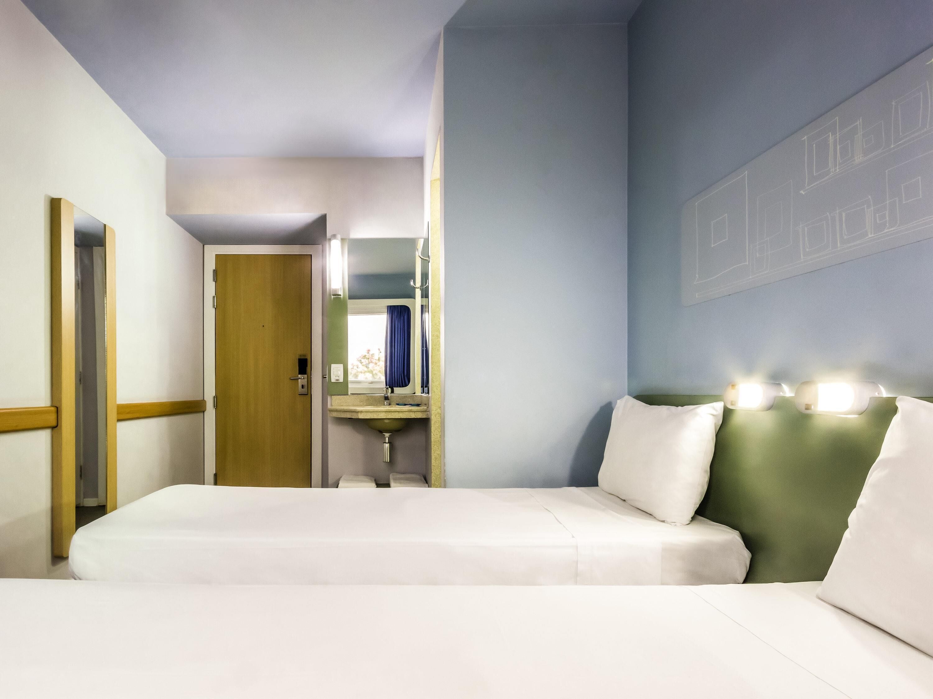 Habitación de hotel con cama, baño con espejo, lavabo y puerta que da a otra habitación.